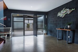 Ein modernes Interieur mit Betonboden, einer Holzbank, einer Glastür, die nach draußen führt, und einer dunkel verputzten Ziegelwand mit Fisch-Wandbild.