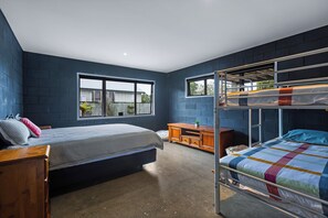 Ein Schlafzimmer mit Etagenbett, einem Einzelbett, einer hölzernen Kommode und einem Fenster.