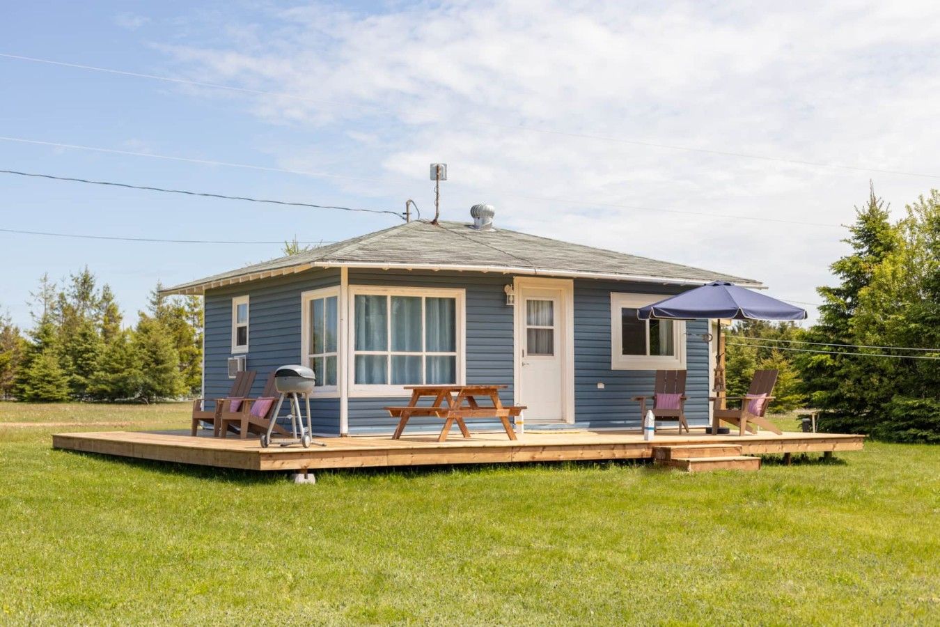 A small, single-story cabin with a porch, a grill, and outdoor seating.