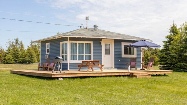 Eine kleine, eingeschossige Holzhütte mit Veranda, Grill und Gartenmöbeln.