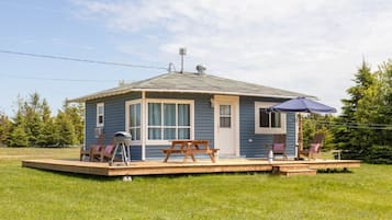 A small, single-story cabin with a porch, a grill, and outdoor seating.