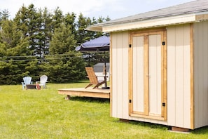 A wooden shed with a door, a deck, and two Adirondack chairs.