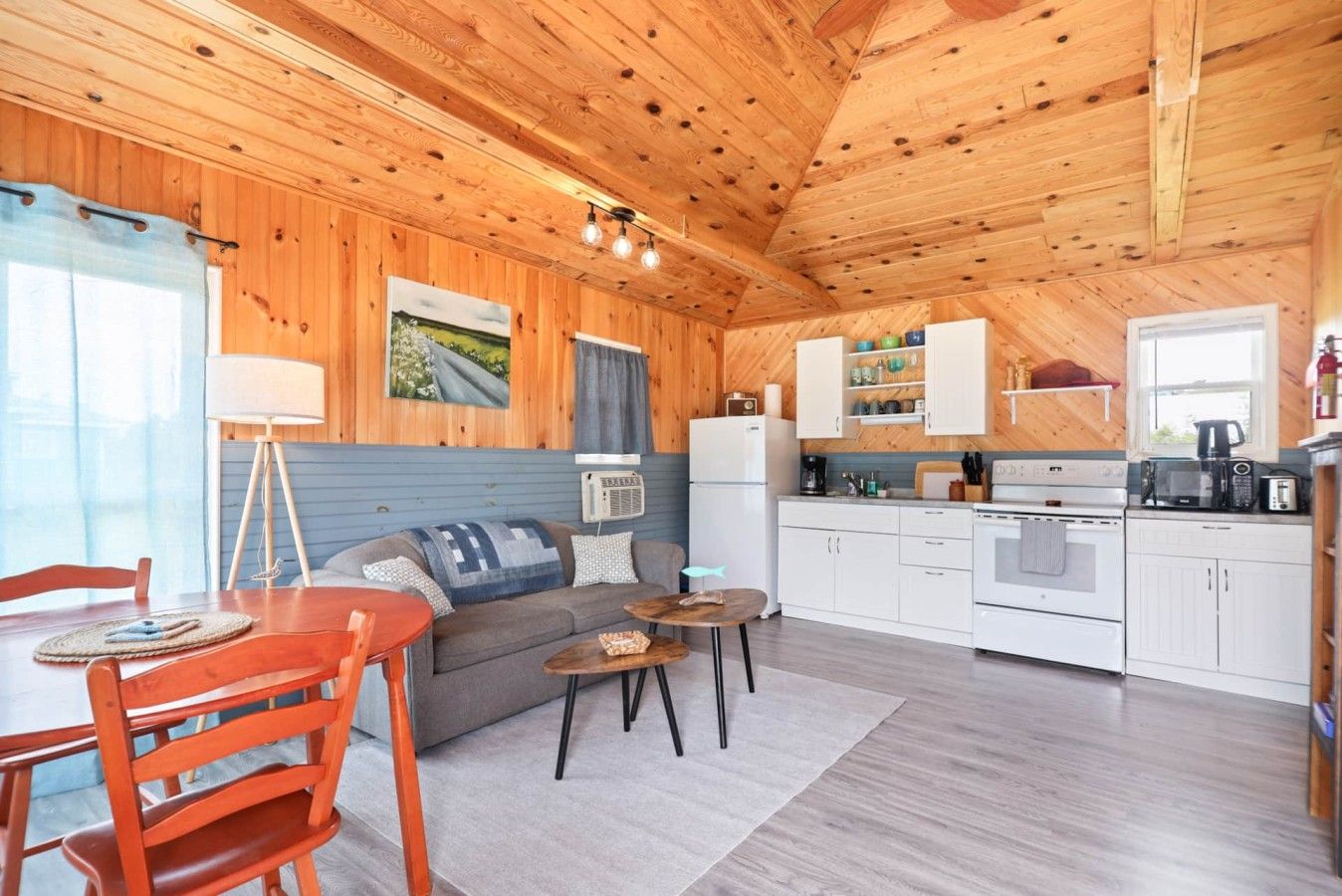 A cozy cabin interior with a dining area, sofa, kitchen, and a window with curtains.