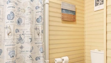 A bathroom with a nautical-themed shower curtain, a toilet, and a small shelf with a magazine.