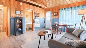 Ein gemütliches Blockhaus-Interieur mit Holzbalkendecke, Essbereich, einer Couch und einem Bett mit Streifenoptik.