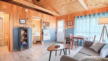 A cozy cabin interior with a wooden ceiling, a dining area, a sofa, and a bed with a striped blanket.
