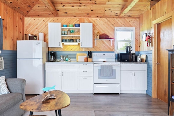 A compact kitchen with white cabinets, a refrigerator, a stove, and a microwave.