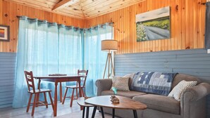 Ein gemütliches Zimmer mit Holzbalkendecke, einer Couch mit gemusterten Kissen, einem kleinen Tisch und einem Esstisch mit Stühlen.