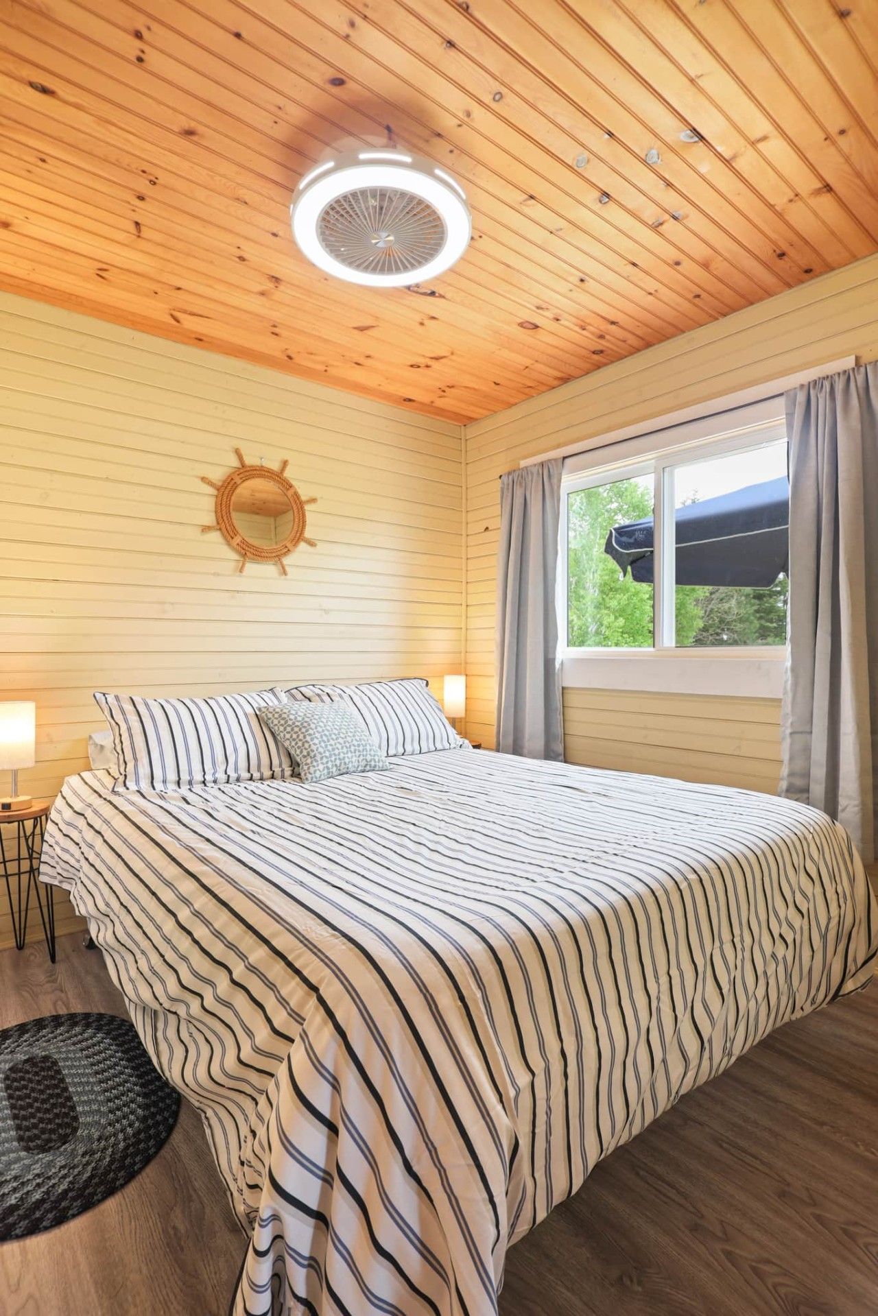 A bedroom with a bed, a round wall clock, a window with curtains, and a ceiling fan.