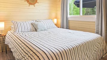 A bedroom with a bed, a round wall clock, a window with curtains, and a ceiling fan.