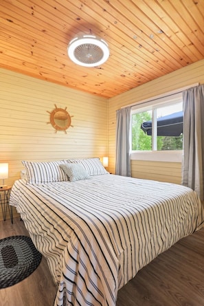 Quarto com cama, relógio de parede redondo, janela com cortinas e ventilador de teto.