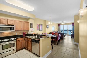 A kitchen with wooden cabinets, a microwave, a stove, and a dishwasher. There is a dining area with a table and chairs. - Sunrise Beach #1609 (Panama City Beach)