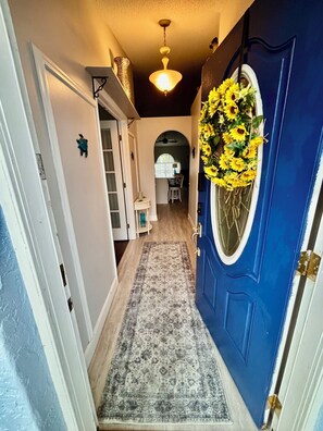 A hallway with a blue door, a patterned rug, and a decorative sunflower garland. - Spacious Pet Friendly 4-bedroom home in Port St. Lucie with pool & fenced yard (Port St. Lucie)