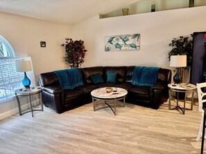 A living room with a black leather sofa, a round coffee table, and a small side table with a lamp. - Spacious Pet Friendly 4-bedroom home in Port St. Lucie with pool & fenced yard (Port St. Lucie)
