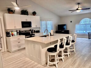 A modern kitchen with white cabinetry, a central island with bar stools, a microwave, a toaster, and a ceiling fan. - Spacious Pet Friendly 4-bedroom home in Port St. Lucie with pool & fenced yard (Port St. Lucie)