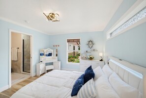 Ein Schlafzimmer mit Bett, Schminktisch, Kommode und einem Fenster mit Blick auf Grünflächen.