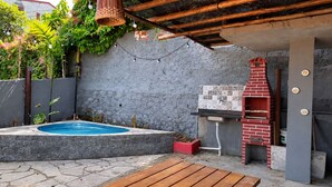 Quintal com piscina, um banco de madeira, churrasqueira de tijolos e painel de azulejos.