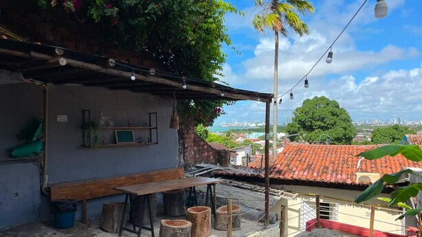 Área de varanda externa com mesa e banquetas de madeira, uma piscina pequena e vista para a cidade.