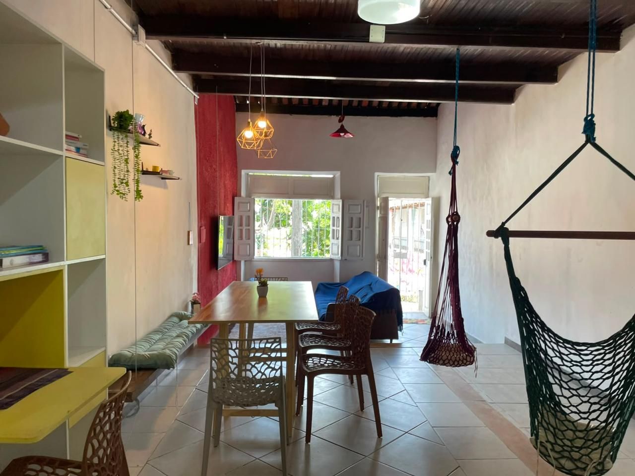 Quarto com mesa de jantar, cadeiras, uma rede e vista para o exterior.
