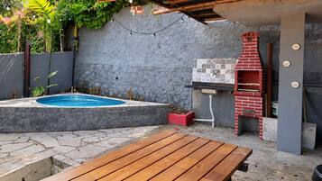 Un pati d'era amb piscina, una banca de fusta, una barbacoa de rajola i un frontal de rajoles.