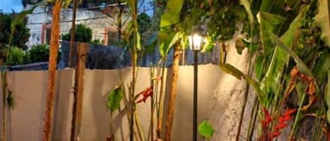 Zona de piscina con borde de piedra, rodeada de plantas y una pérgola a rayas.
