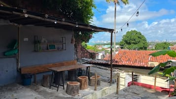 Área de varanda externa com mesa e banquetas de madeira, uma piscina pequena e vista para a cidade.