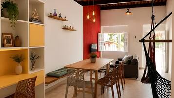 Uma área de jantar com mesa e cadeiras de madeira, parede com destaque em vermelho e uma cadeira suspensa.