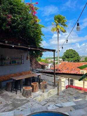 An outdoor seating area with a pool, wooden stools, and a view of the cityscape. - Olinda sitio histórico - Loctemp (Olinda)
