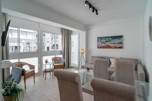 Ein modernes Wohnzimmer mit einer Couch, Sesseln, einem Glastisch und einem Bild an der Wand.