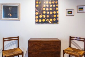 Ein Zimmer mit zwei Holzstühlen, einem kleinen Holztisch und drei gerahmten Kunstwerken an der Wand.
