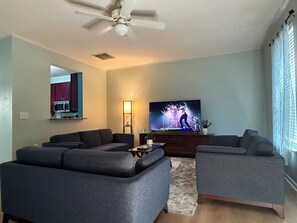 A living room with a flat-screen TV, two grey sofas, a coffee table, a floor lamp, and a ceiling fan. - 3-bedroom townhome in perfect Cary Downtown with cool AC and comfort. (Cary)