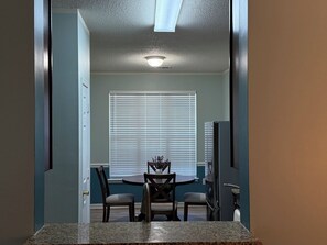 Un espace repas comprenant une table, des chaises, un luminaire au plafond et une fenêtre avec des stores.