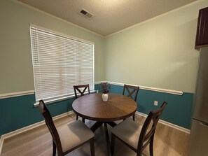 A dining area with a round table, four chairs, a vase with flowers, and a window with blinds. - 3-bedroom townhome in perfect Cary Downtown with cool AC and comfort. (Cary)