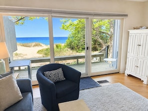 A room with a view of the beach, a dark blue armchair, a white cabinet, and a small table. - Lake Michigan Beachfront | Fireplace + Lake Views (Glen Arbor)