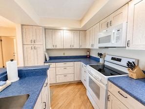 A kitchen with wooden cabinets, a microwave, an oven, and a blue countertop. - Lake Michigan Beachfront | Fireplace + Lake Views (Glen Arbor)