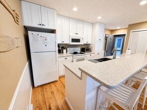 A modern kitchen with white cabinets, a refrigerator, a microwave, an oven, and a granite countertop. - Glen Arbor Waterfront | Lake Views + Fireplace (Glen Arbor)