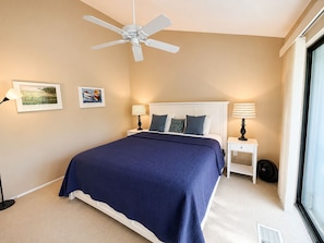 A bedroom with a bed, a ceiling fan, two bedside lamps, a window, and two framed pictures on the wall. - Glen Arbor Waterfront | Lake Views + Fireplace (Glen Arbor)
