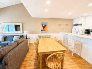 A cozy living area with a sofa, a dining table with chairs, a kitchen with white cabinets, and a painting on the wall. - Glen Arbor Waterfront | Lake Views + Fireplace (Glen Arbor)