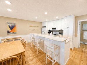 A compact kitchen with white cabinets, a central island with bar stools, and a dining table with chairs. - Glen Arbor Waterfront | Lake Views + Fireplace (Glen Arbor)