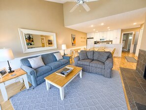 A living room with a sofa, a coffee table, and a dining area with chairs. - Glen Arbor Waterfront | Lake Views + Fireplace (Glen Arbor)