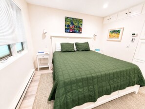 A bedroom with a bed, nightstand, and a painting on the wall. - Lake Michigan Beachfront | Private Deck + King Bed (Glen Arbor)