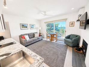 Ein modernes Wohnzimmer mit einem grauen Sofa, einem Esstisch mit Stühlen, einem Kamin und einer Küchenzeile mit einer Granitarbeitsplatte und Spüle.