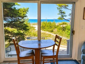 Ein Zimmer mit einer Schiebetür zu einer Terrasse, auf der sich ein Tisch und Stühle befinden, mit Blick auf einen Strand und das Meer.