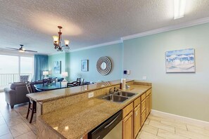 A modern kitchen with granite countertops, a dishwasher, and a dining area with a table and chairs. - Ocean Reef 1703- Ocean O'peace (Panama City Beach)
