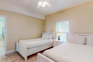 A bedroom with two single beds, a nightstand with a lamp, a ceiling fan, and a window with blinds. - Ocean Reef 1703- Ocean O'peace (Panama City Beach)
