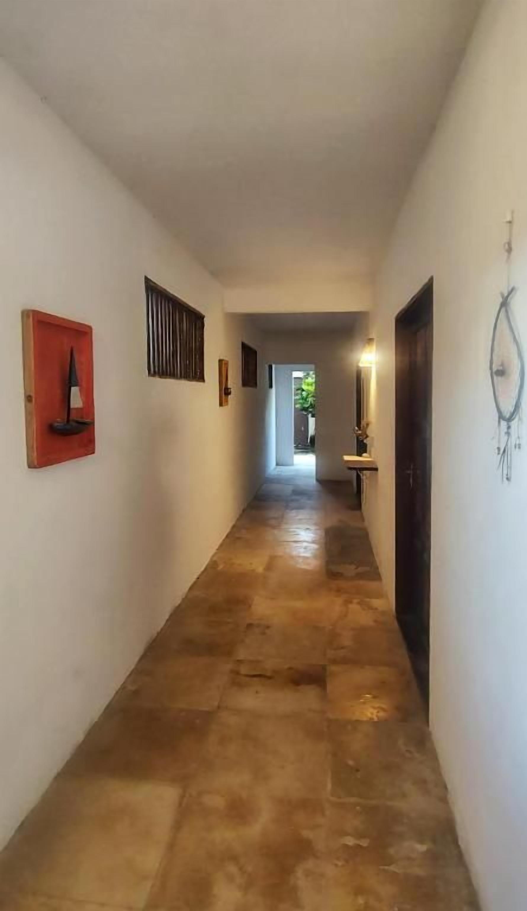 Un pasillo con suelo de baldosas, una puerta a la derecha y un aplique en la pared.