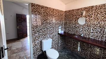 A bathroom with a tiled wall, a toilet, a sink, and a mirror.