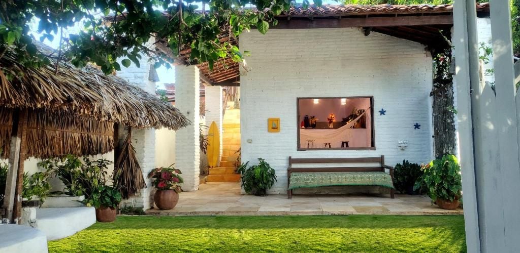 Un edificio blanco con estructura de techo de paja, un banco y plantas en macetas.