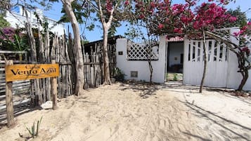 Una entrada arenosa a una propiedad con un letrero de madera que dice 'Casa Vento Azul' y un edificio blanco con un celosía.