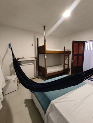 Une chambre avec un lit superposé, un bureau, une chaise, un hamac, un radiateur et une porte.